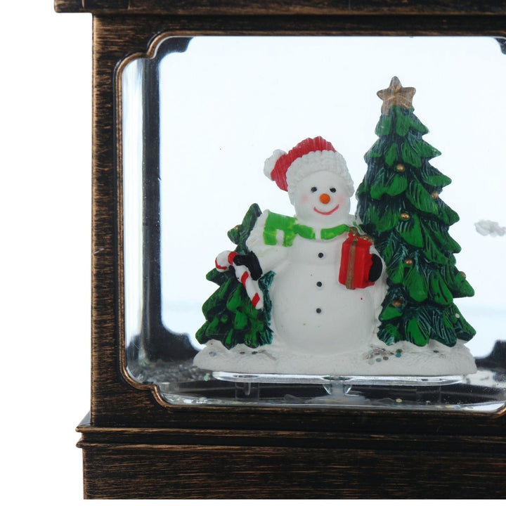 Decorative snowman with a tree and gift in a glass lantern display case.