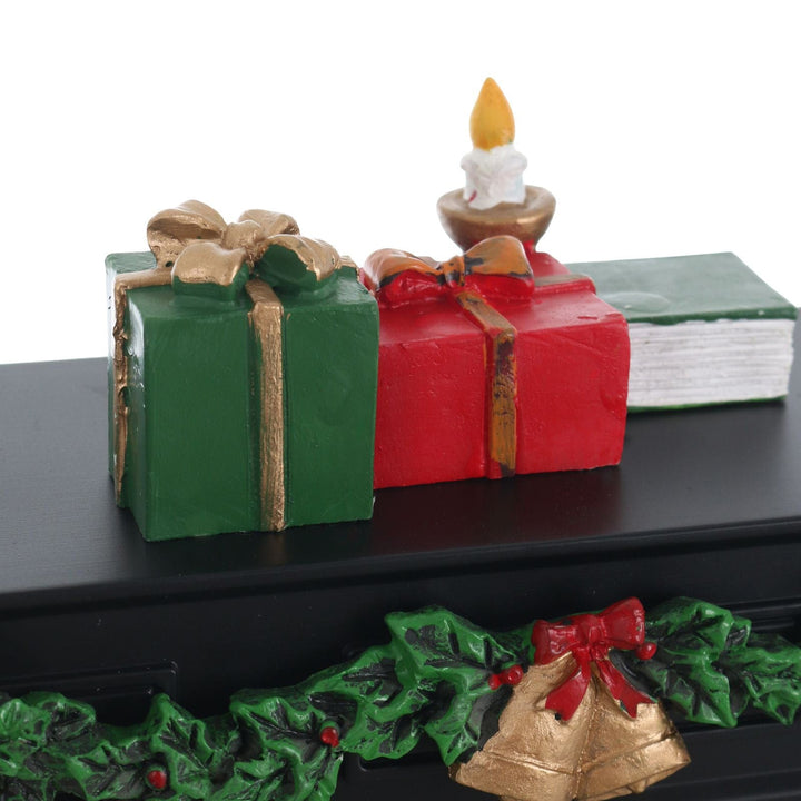 Decorative Christmas scene with green and red presents, a candle, and holly leaves on a black surface.