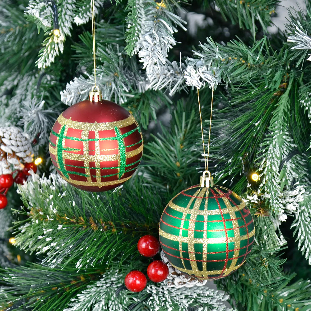 Two green and red tartan Christmas baubles hanging on a decorated tree.