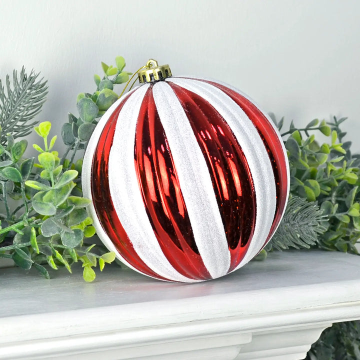 Very large red and white striped Christmas tree bauble on a white mantelpiece with green Christmas garland