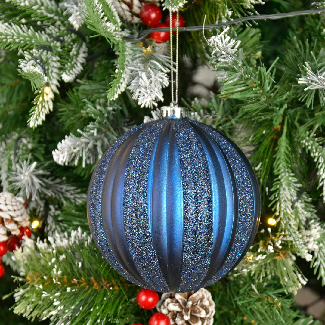 Extra large blue glittery Christmas tree bauble ornament on a decorated tree