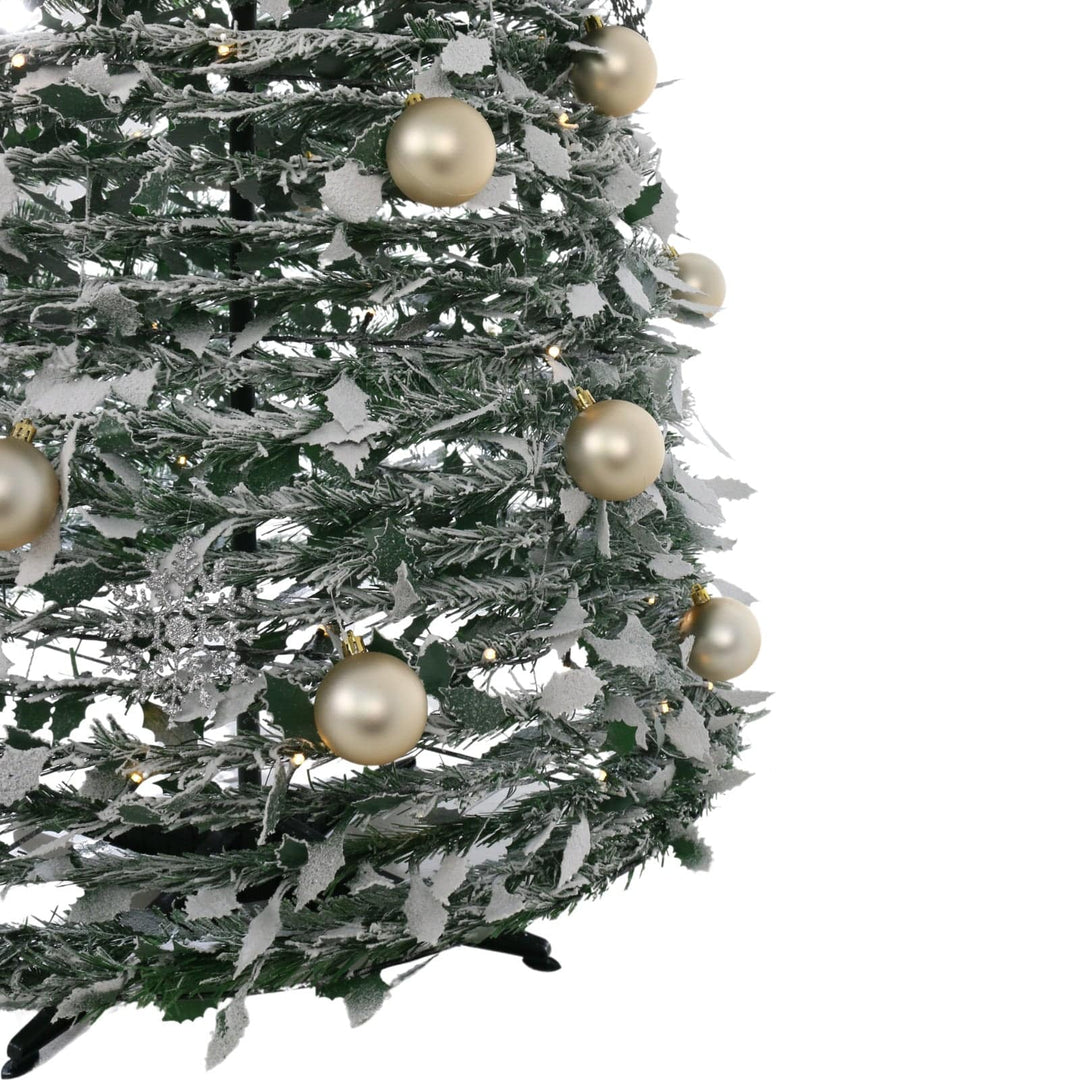 close up of christmas tree base with gold baubles and holly leaves covered with snow
