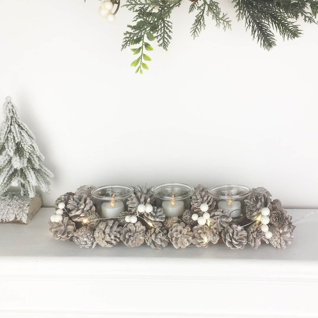 Decorative candle holder with pinecones and candles on a white surface with Christmas decorations.