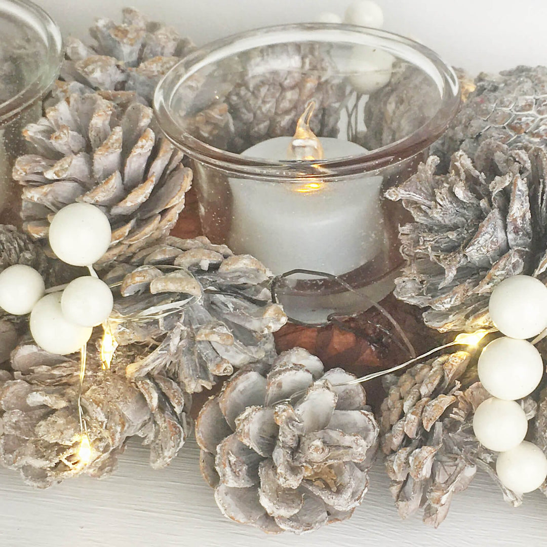 Decorative arrangement with pinecones, a candle, and string lights on a light background