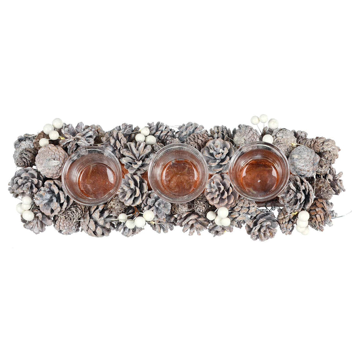 Overhead view of a Christmas candle holder with three glass jars pine cones and white berries