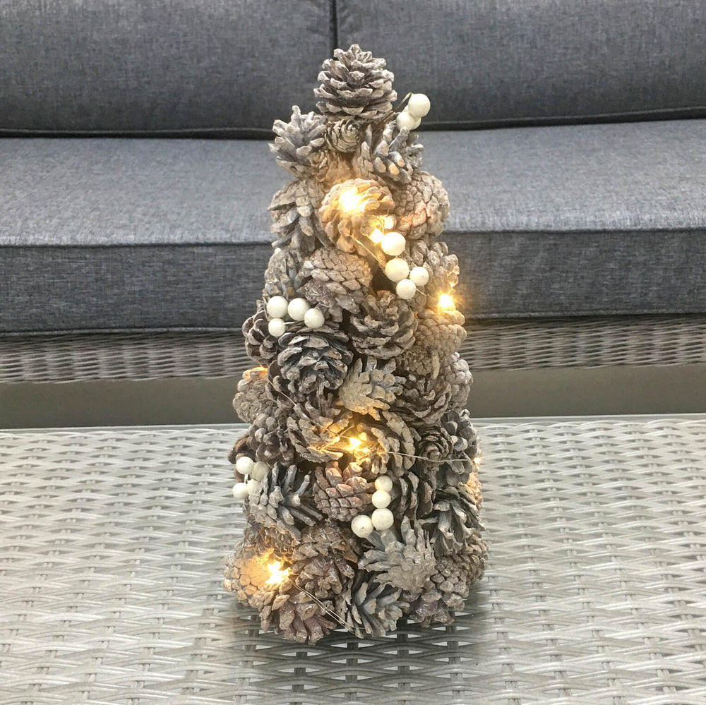 Small pine cone Christmas tree with lights on a glass topped grey wicker table