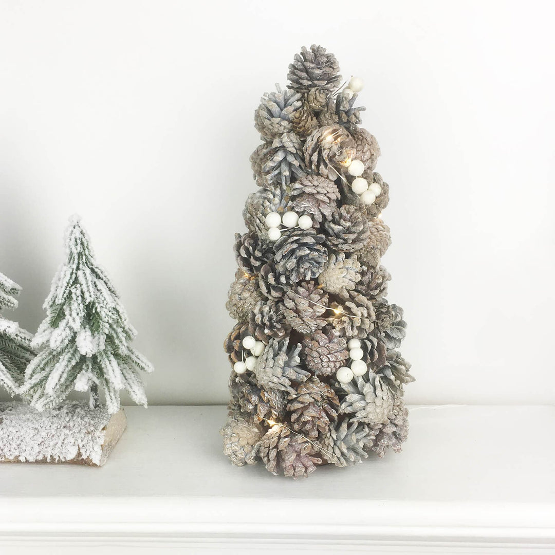 Pine cone Christmas tree with snowberries on a mantelpiece with snow flocked fir tree