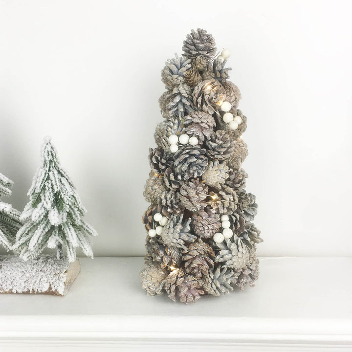 Pine cone Christmas tree with snowberries on a mantelpiece with snow flocked fir tree