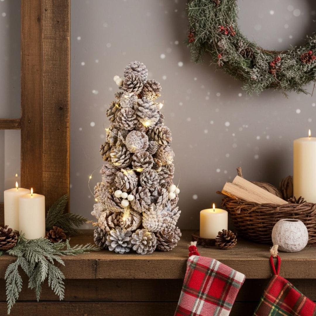 Decorative pine cone tree with lights on a wooden mantel with candles and a wreath in the background.