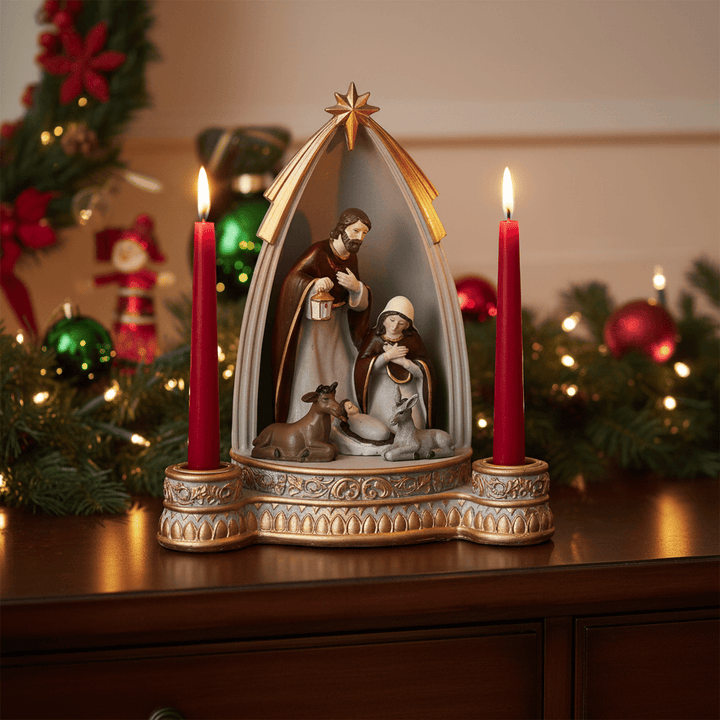 Decorative nativity scene with two lit red candles on a wooden surface, surrounded by Christmas decorations.