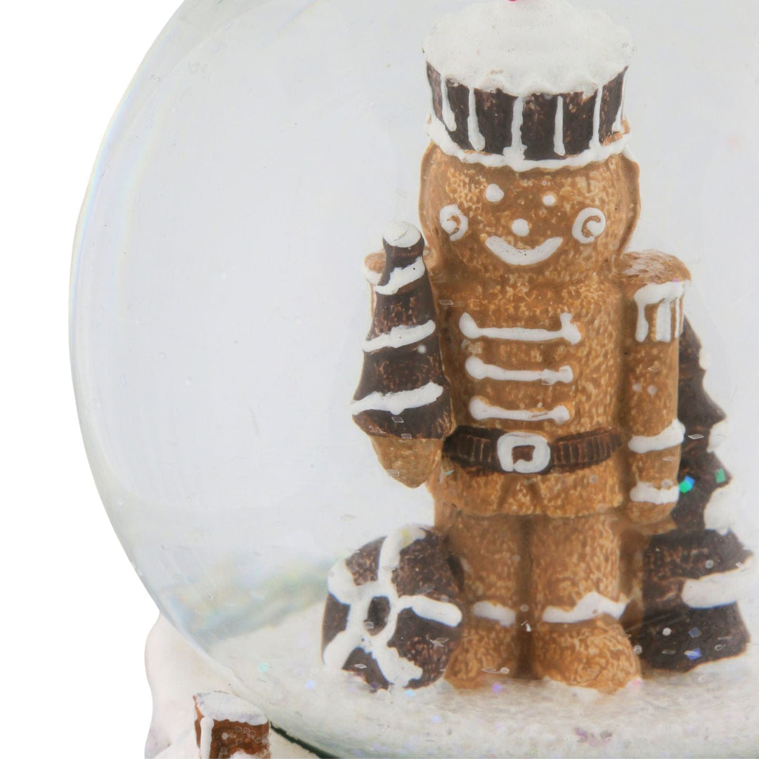 Gingerbread nutcracker man holding christmas tree inside snow globe with a white background