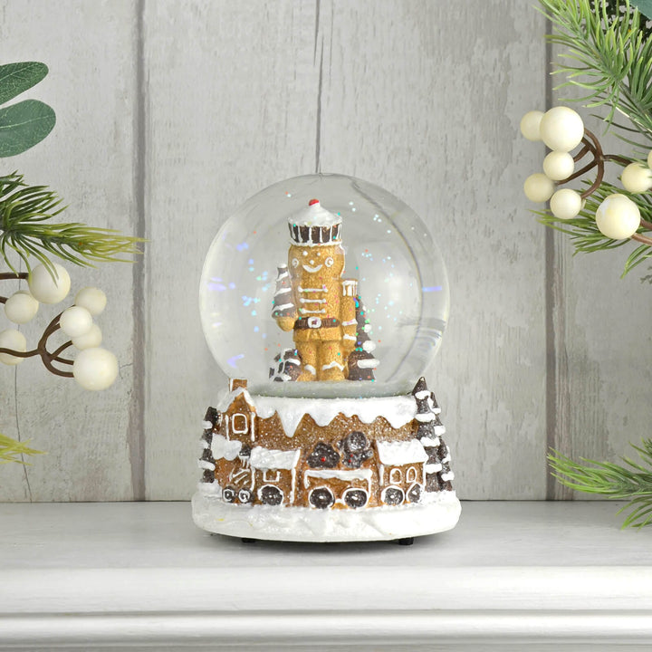 Gingerbread man nutcracker snow globe with train on a wooden surface with Christmas foliage.