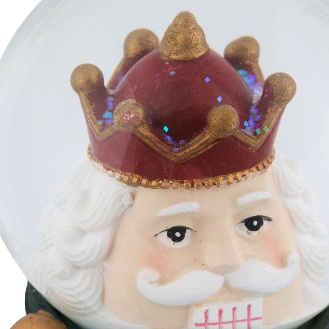 Decorative figure of a nut cracker with a crown inside a snow globe on a white background