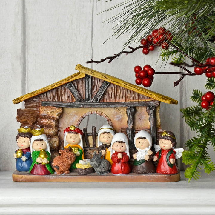 Nativity scene figurine set with a rustic stable and colourful characters on a mantelpiece with Christmas foliage