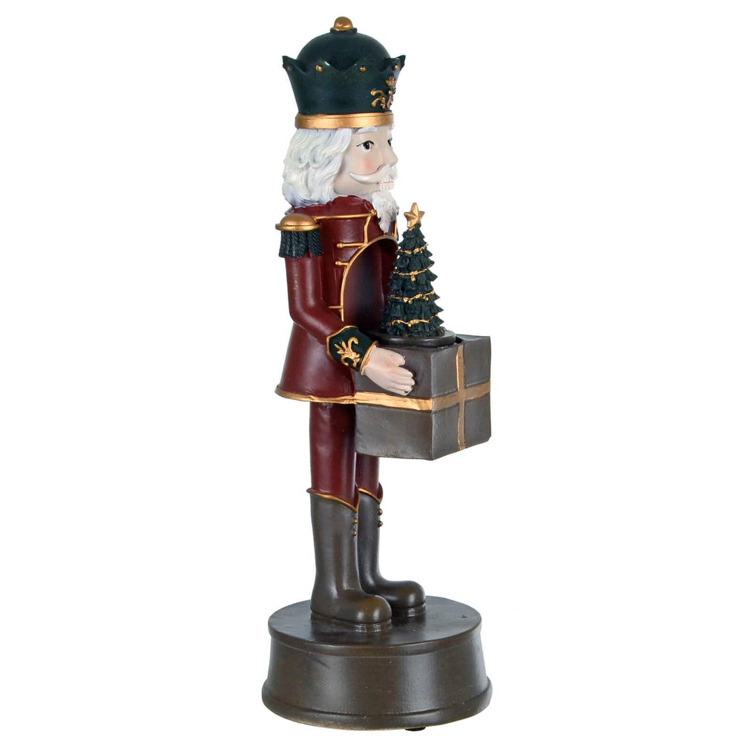 Decorative nutcracker figure holding a gift and small tree on a white background