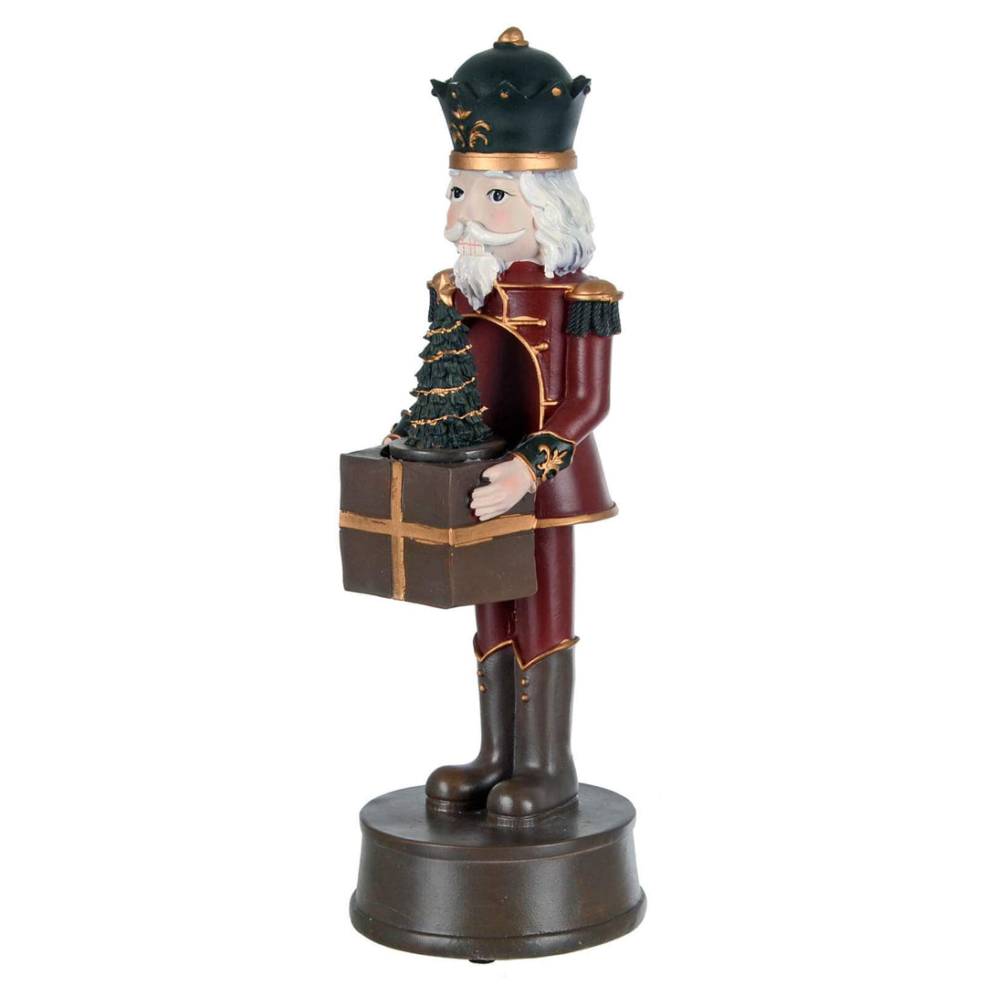 Side view of a nutcracker Christmas figure holding a present and Christmas tree