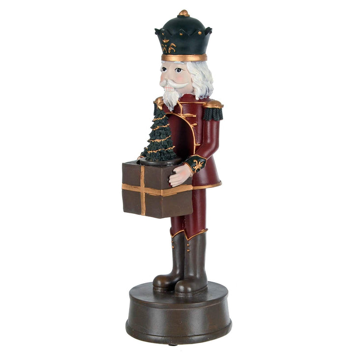 Side view of a nutcracker Christmas figure holding a present and Christmas tree
