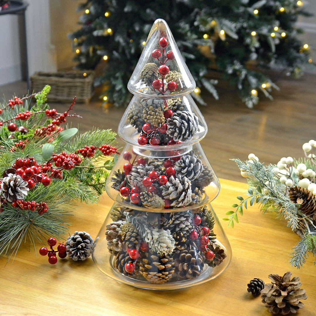 christmas tree storage jar on wooden coffee table with tree in background, filled with pine cones and red berry clusters