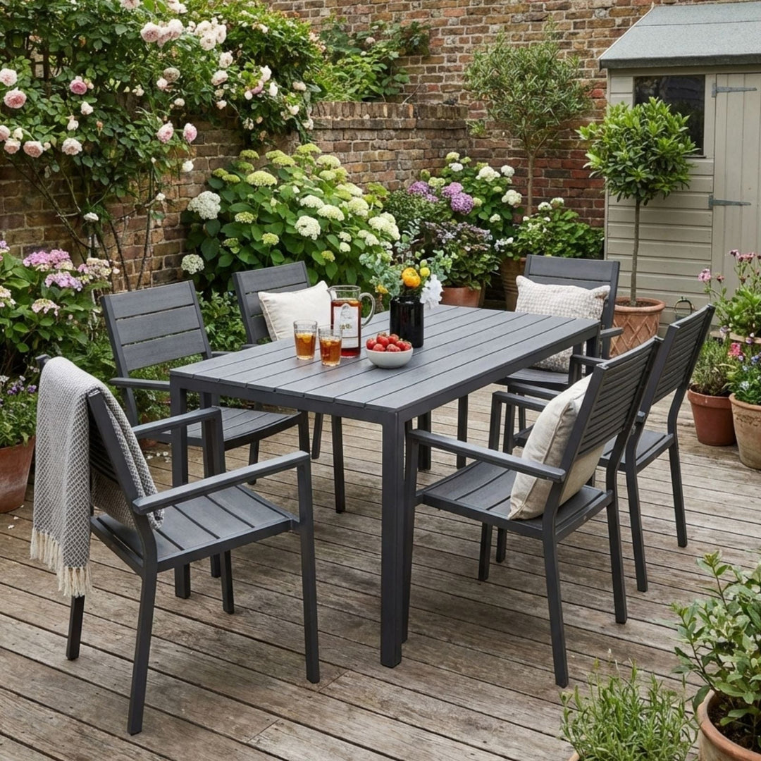 Outdoor dining set with a table and chairs on a wooden deck, surrounded by flowers and plants.