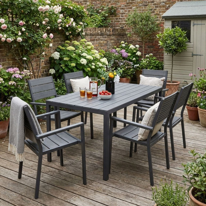 Outdoor dining set with a table and chairs on a wooden deck, surrounded by flowers and plants.