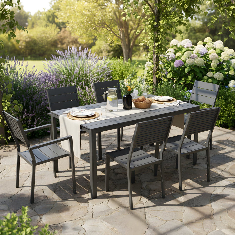 Outdoor dining setup with a table and chairs on a stone patio surrounded by greenery.